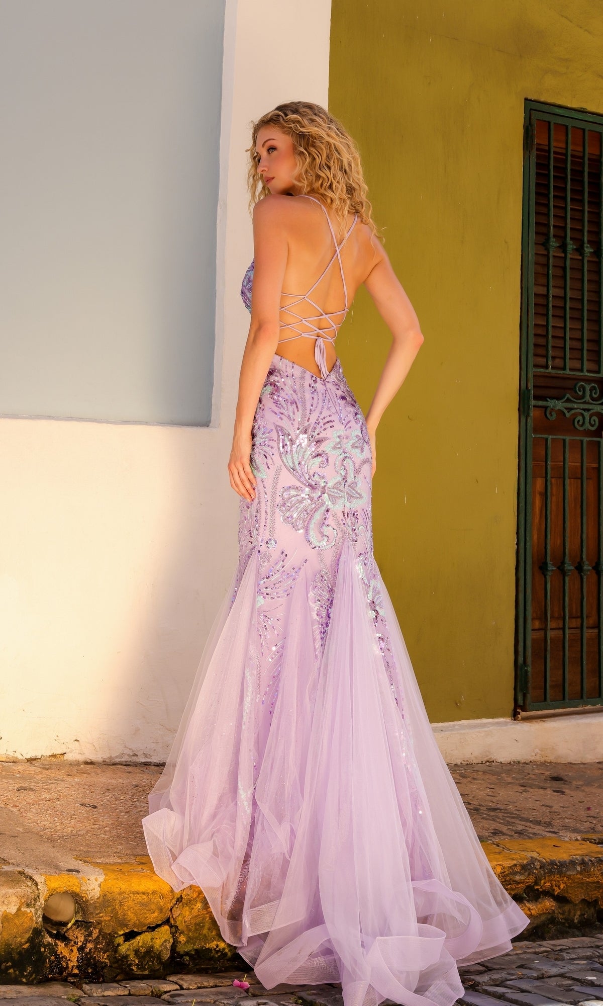 A woman wearing the Nox Anabel Tight Sequin Mermaid Prom Dress C1416 stands on a sunlit street near a green door and two-tone wall.